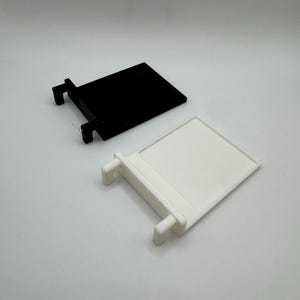 May include: Two plastic shelf brackets, one black and one white. The brackets have a rectangular shape with two small tabs on the side.