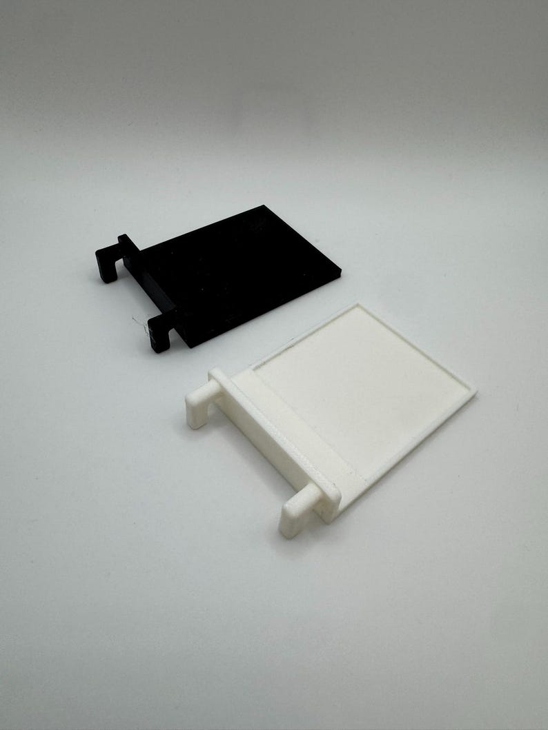 May include: Two plastic shelf brackets, one black and one white. The brackets have a rectangular shape with two small tabs on the side.
