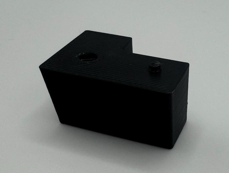 May include: A black plastic corner bracket with two holes. The bracket is designed to connect two pieces of wood or other materials at a 90-degree angle.