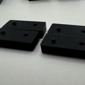May include: Four black plastic rectangular blocks, each with two holes. The blocks are arranged in two pairs, with the holes facing each other.