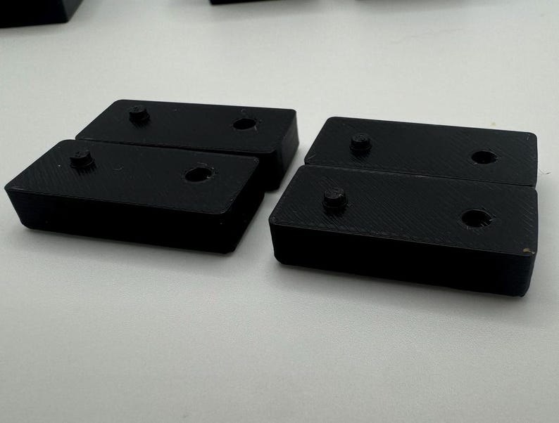 May include: Four black plastic rectangular blocks, each with two holes. The blocks are arranged in two pairs, with the holes facing each other.