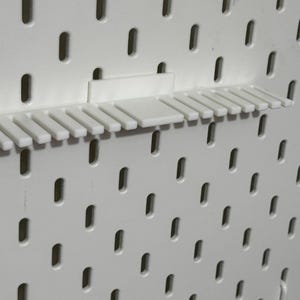 K&ouml;nnte beinhalten: Eine wei&szlig;e Lochwand mit einem wei&szlig;en Kunststoffregal mit 15 F&auml;chern zum Organisieren von Werkzeugen oder anderen Gegenst&auml;nden.