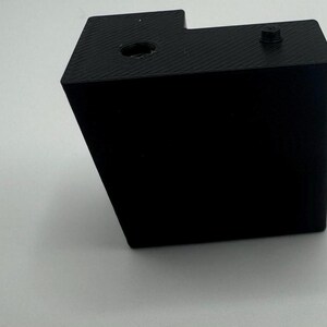 May include: A black plastic box with a small hole on the top and a screw on the side.