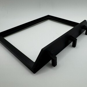 May include: Black plastic frame with three small hooks on the bottom. The frame is designed to stand upright.