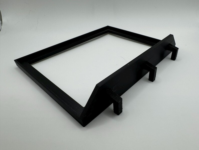 May include: Black plastic frame with three small hooks on the bottom. The frame is designed to stand upright.