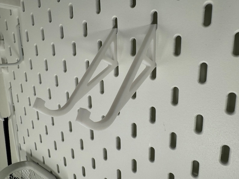 May include: Two white plastic shelf brackets mounted on a white pegboard wall.