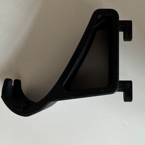 May include: Black plastic wall mount bracket with a triangular shape and a hook on the side.