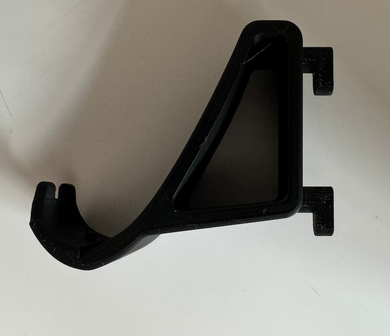 May include: Black plastic wall mount bracket with a triangular shape and a hook on the side.