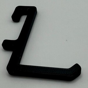 May include: A black plastic hook with a curved shape. The hook is designed to hang items on a wall or other surface.