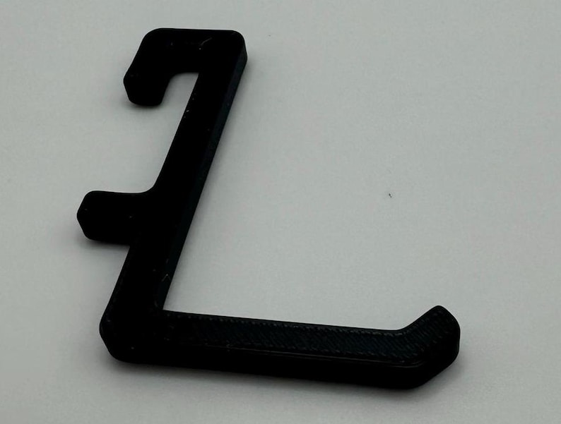 May include: A black plastic hook with a curved shape. The hook is designed to hang items on a wall or other surface.