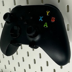 May include: A black Xbox controller with a white background. The controller has four buttons labeled A, B, X, and Y. The buttons are colored green, red, blue, and yellow.