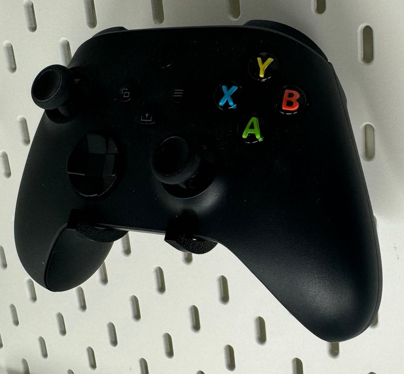 May include: A black Xbox controller with a white background. The controller has four buttons labeled A, B, X, and Y. The buttons are colored green, red, blue, and yellow.