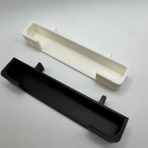 May include: Two rectangular, open-top containers. One is black, the other is white. Both have a similar design with a long, narrow shape and a lip on each end. The black container has a small, cylindrical protrusion on one side.