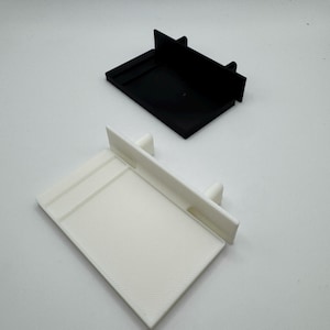 May include: Two 3D printed plastic shelf brackets, one white and one black. The brackets are designed to be used for shelves or other objects.