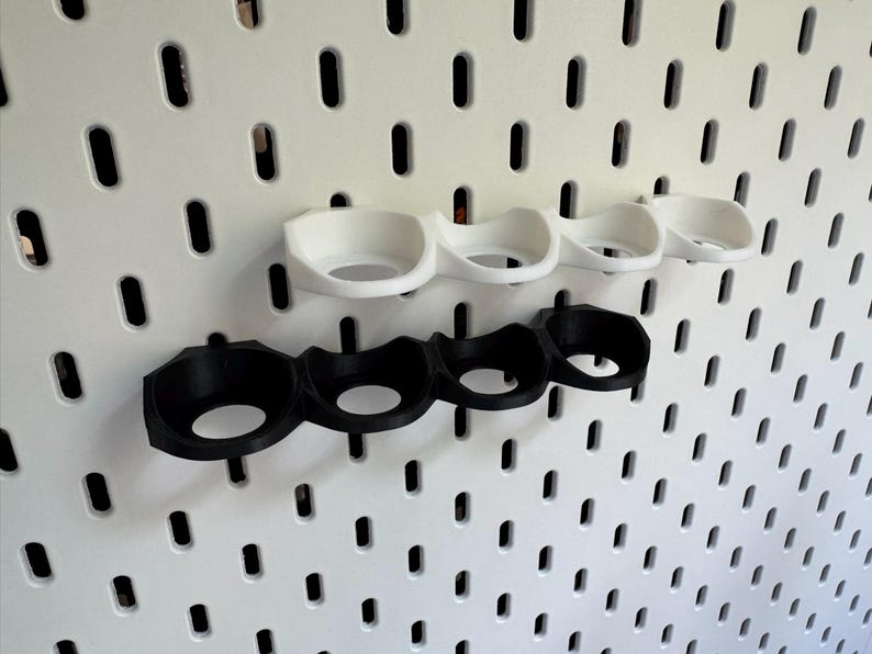 Puede incluir: Dos juegos de portavasos, uno negro y uno blanco, montados en una pared de tablero de clavijas. Cada juego tiene cuatro portavasos.