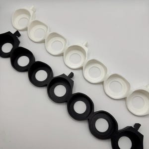 以下が含まれることがあります： 中央に円形の穴が開いた黒と白のプラスチック製のリングが2セット。リングはチェーン状に繋がっています。
