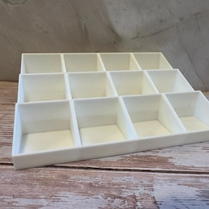 Peut inclure: Un organisateur de bijoux blanc &agrave; plusieurs compartiments. L'organisateur est fait d'un mat&eacute;riau lisse et solide et est con&ccedil;u pour contenir divers petits objets. Les compartiments sont dispos&eacute;s en gradins.