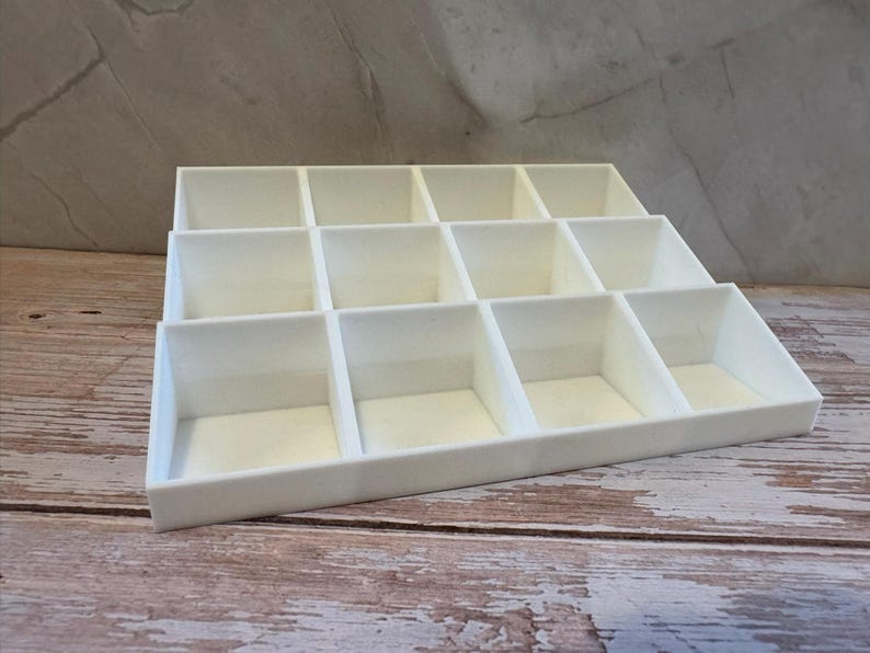 Peut inclure: Un organisateur de bijoux blanc &agrave; plusieurs compartiments. L'organisateur est fait d'un mat&eacute;riau lisse et solide et est con&ccedil;u pour contenir divers petits objets. Les compartiments sont dispos&eacute;s en gradins.