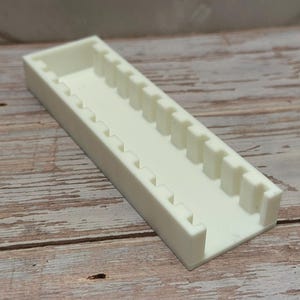 Puede incluir: Un organizador rectangular de pl&aacute;stico blanquecino con una serie de divisores verticales. El organizador est&aacute; colocado sobre una superficie de madera, mostrando su dise&ntilde;o y uso potencial para organizar objetos peque&ntilde;os.
