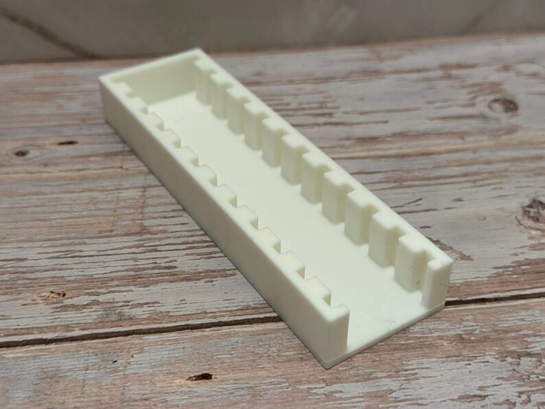 Puede incluir: Un organizador rectangular de pl&aacute;stico blanquecino con una serie de divisores verticales. El organizador est&aacute; colocado sobre una superficie de madera, mostrando su dise&ntilde;o y uso potencial para organizar objetos peque&ntilde;os.