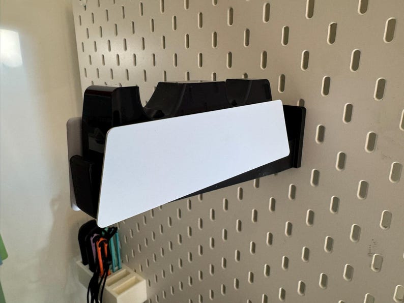 K&ouml;nnte beinhalten: Ein schwarz-wei&szlig;er Wandorganizer mit einem wei&szlig;en, abgewinkelten Regal. Der Organizer ist an einer Lochwand befestigt. Darunter befinden sich mehrere farbige Gegenst&auml;nde.