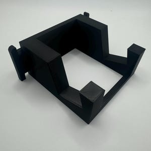 K&ouml;nnte beinhalten: Ein schwarzer 3D-gedruckter St&auml;nder f&uuml;r ein Ger&auml;t mit quadratischer Basis und einer erh&ouml;hten Plattform.