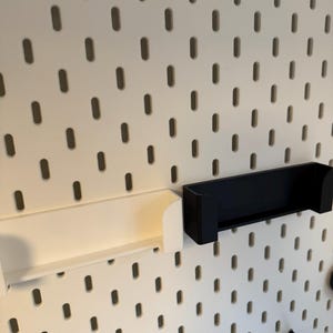 Puede incluir: Panel perforado blanco con agujeros ovalados espaciados uniformemente, con un estante blanco y un estante negro. Los estantes est&aacute;n dise&ntilde;ados para fijarse al panel perforado. El panel perforado es una soluci&oacute;n vers&aacute;til de almacenamiento y organizaci&oacute;n.