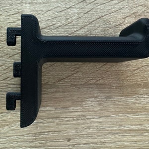 Pu&ograve; includere: Un supporto per cuffie nero, stampato in 3D. Il supporto ha una base a forma di T con tre piccole sporgenze rettangolari e una parte superiore curva per sostenere le cuffie. Il supporto &egrave; realizzato in plastica nera e ha una superficie strutturata.