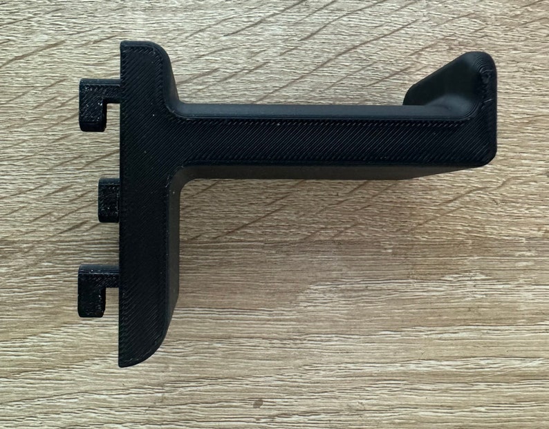 Pu&ograve; includere: Un supporto per cuffie nero, stampato in 3D. Il supporto ha una base a forma di T con tre piccole sporgenze rettangolari e una parte superiore curva per sostenere le cuffie. Il supporto &egrave; realizzato in plastica nera e ha una superficie strutturata.