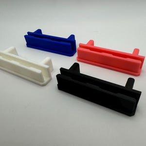 Pode incluir: Quatro suportes de prateleira de pl&aacute;stico em diferentes cores: branco, azul, rosa e preto. Cada suporte tem duas ranhuras e uma borda elevada na parte superior.