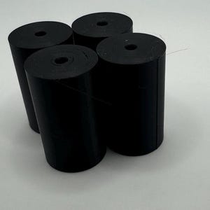 May include: Four black rubber rolls, each with a hole in the center, are stacked on top of each other.