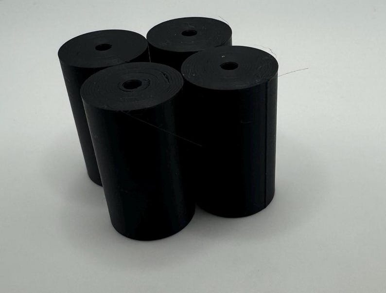 May include: Four black rubber rolls, each with a hole in the center, are stacked on top of each other.