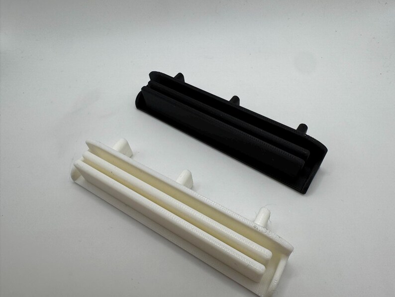 Pode incluir: Dois objetos retangulares de pl&aacute;stico, um preto e outro branco, s&atilde;o exibidos contra um fundo branco. Cada objeto tem um design canelado com pequenas protuber&acirc;ncias. Parecem ser componentes.