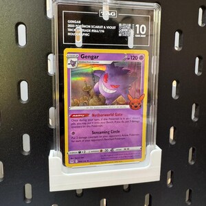 May include: A graded Gengar Pok&eacute;mon card from the 2023 Scarlet & Violet Trick or Trade set, holographic, graded 10 Gem Mint. The card features a purple Gengar character with the text "Gengar" and "120". The card is in a protective case.