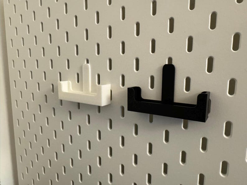 以下が含まれることがあります： 2つのペグボードアクセサリー：白と黒のホルダー。ホルダーは白いペグボードに取り付けられています。ホルダーは、垂直のサポートが付いたU字型のベースを持っています。