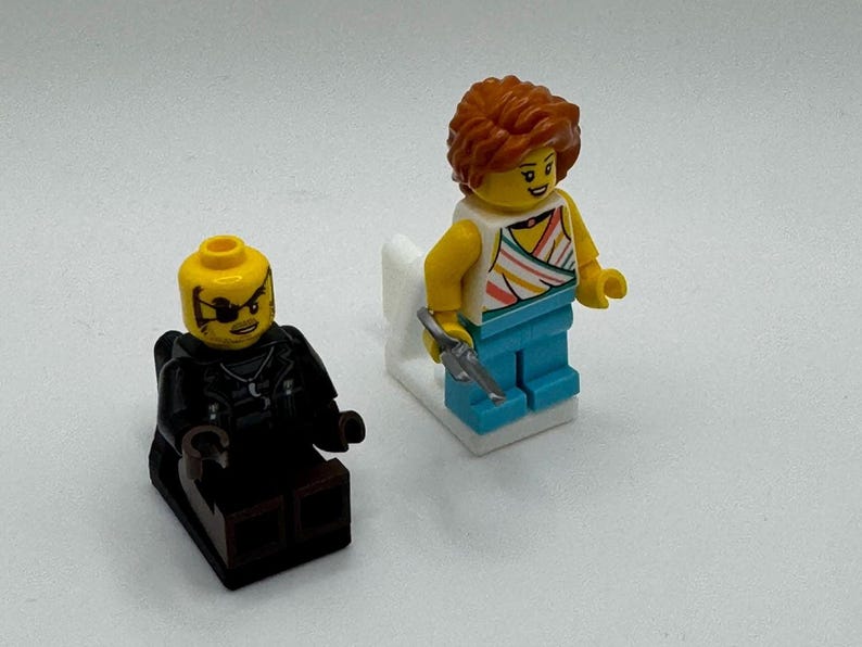 K&ouml;nnte beinhalten: Zwei Lego-Minifiguren. Eine Figur sitzt und tr&auml;gt ein schwarzes Outfit und eine Augenklappe. Die andere Figur steht und tr&auml;gt ein wei&szlig;es Oberteil mit bunten Streifen, eine blaue Hose und h&auml;lt einen silbernen Gegenstand.