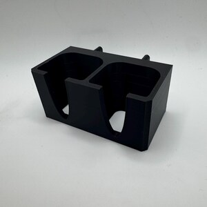 Puede incluir: Un organizador rectangular negro con dos compartimentos. Cada compartimento tiene una abertura curva y una secci&oacute;n elevada en la parte superior. El organizador est&aacute; hecho de un material mate s&oacute;lido.