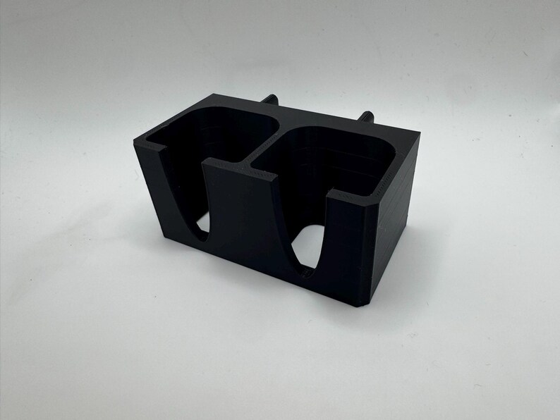 Puede incluir: Un organizador rectangular negro con dos compartimentos. Cada compartimento tiene una abertura curva y una secci&oacute;n elevada en la parte superior. El organizador est&aacute; hecho de un material mate s&oacute;lido.