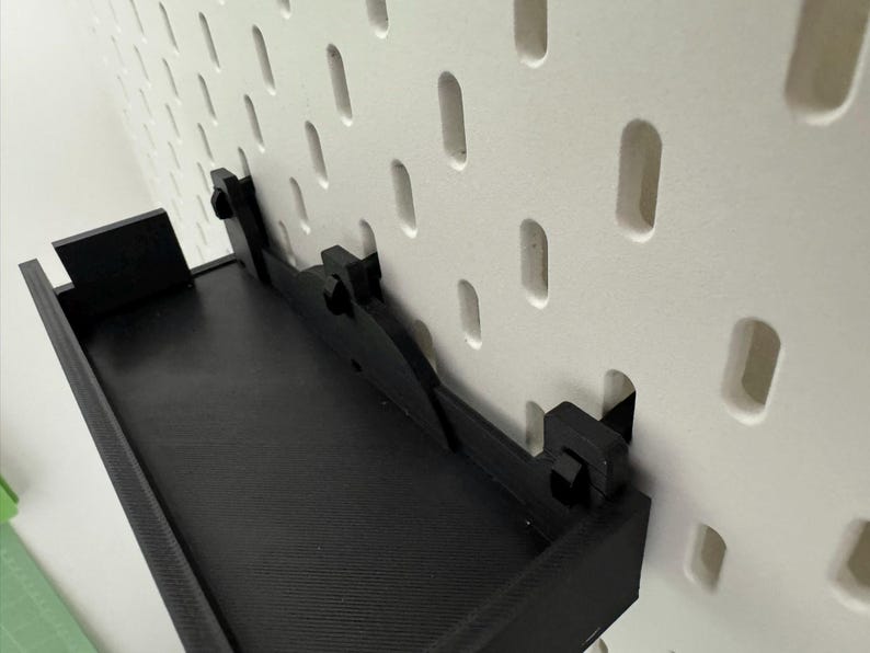 May include: Black wall-mounted shelf with a metal bracket and a pegboard background.