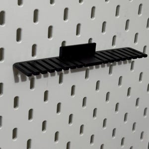 K&ouml;nnte beinhalten: Schwarzer Kunststoff-Pegboard-Organizer mit mehreren Steckpl&auml;tzen zum Aufbewahren von Werkzeugen oder anderen Gegenst&auml;nden.