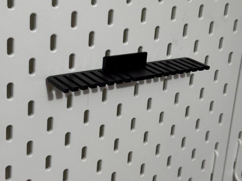 K&ouml;nnte beinhalten: Schwarzer Kunststoff-Pegboard-Organizer mit mehreren Steckpl&auml;tzen zum Aufbewahren von Werkzeugen oder anderen Gegenst&auml;nden.