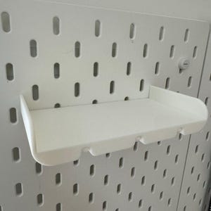 May include: White plastic shelf with a curved front edge, designed to fit into a pegboard wall.