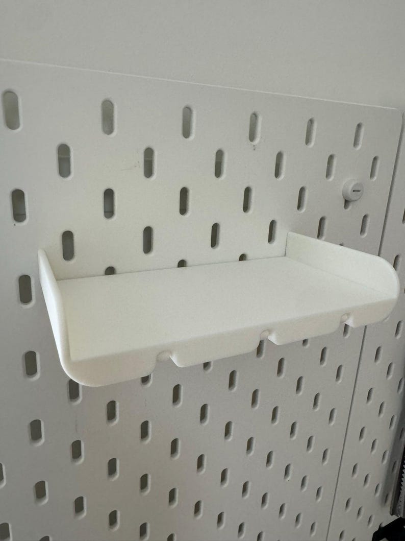 May include: White plastic shelf with a curved front edge, designed to fit into a pegboard wall.