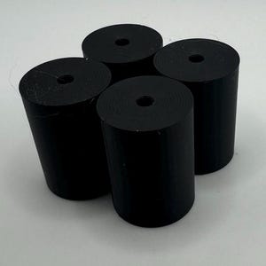 May include: Four black cylindrical objects with a hole in the center. The objects are made of a smooth, matte material.