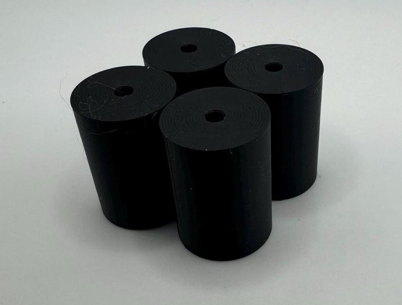 May include: Four black cylindrical objects with a hole in the center. The objects are made of a smooth, matte material.
