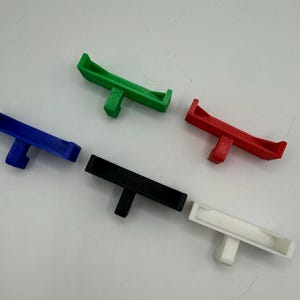 May include: Five 3D printed plastic hooks in different colours: green, blue, black, white, and red. The hooks are designed to be mounted on a wall or other surface.