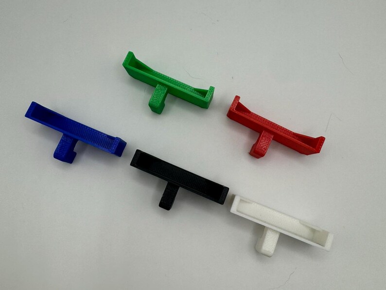 May include: Five 3D printed plastic hooks in different colours: green, blue, black, white, and red. The hooks are designed to be mounted on a wall or other surface.