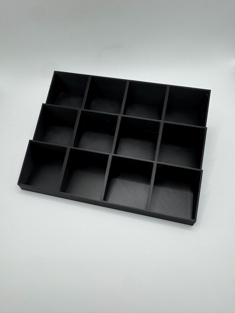 Peut inclure: Un organisateur noir &agrave; plusieurs niveaux avec seize compartiments individuels. L'organisateur est fait d'un mat&eacute;riau noir mat et est con&ccedil;u pour contenir de petits objets. Les compartiments sont dispos&eacute;s en quatre rang&eacute;es et quatre colonnes.
