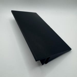 Puede incluir: Una estanter&iacute;a de pl&aacute;stico negro con un ligero &aacute;ngulo, dise&ntilde;ada para sostener objetos en un escritorio o encimera.