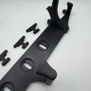 May include: A black 3D-printed stand with a long, flat base featuring three oval cutouts. The stand has a curved support and several small, H-shaped pieces. The items are arranged on a white surface.